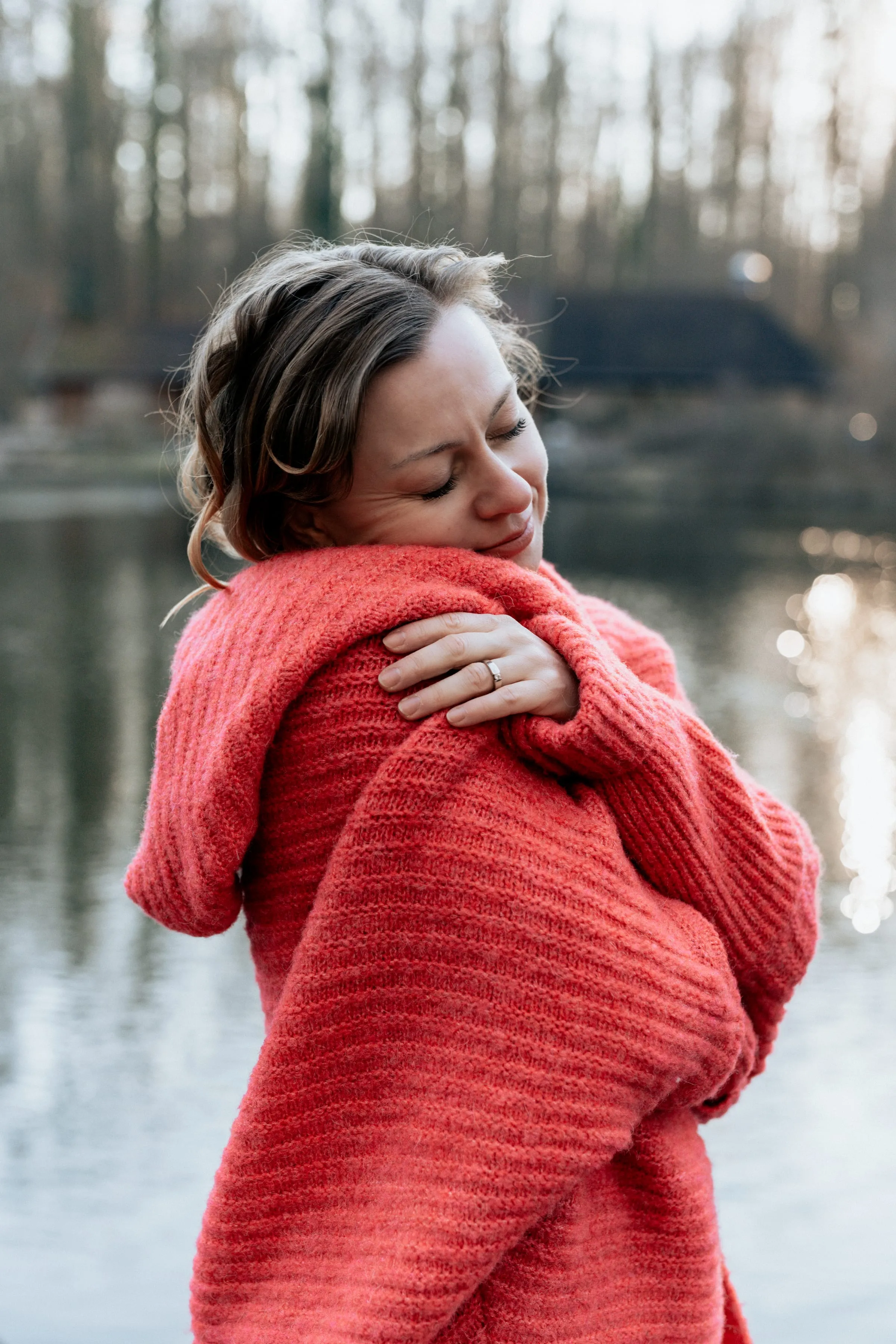 Lidia Baer, Selbstumarmung am See, Augen geschlossen, roter Pullover – persönlich und emotional